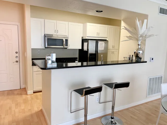 a kitchen with stainless steel appliances kitchen island granite countertop a refrigerator a stove and white cabinets with wooden floor