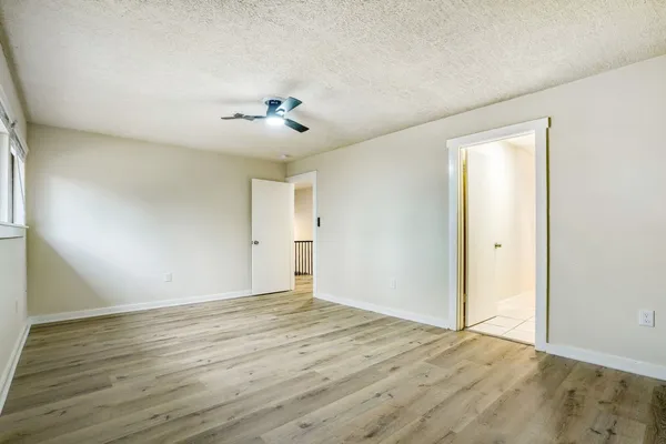 a view of an empty room with wooden floor and a ceiling fan
