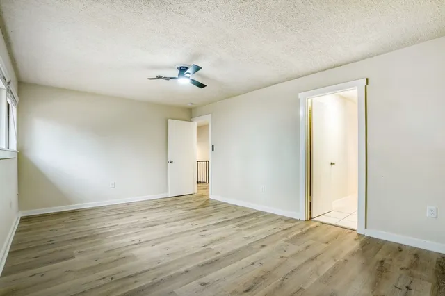 a view of an empty room with wooden floor and a ceiling fan
