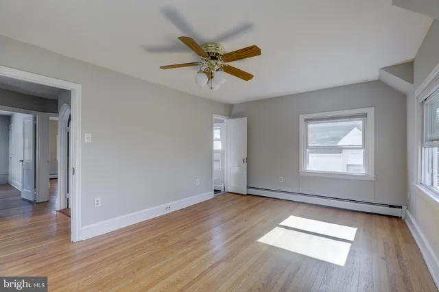 an empty room with wooden floor a ceiling fan and windows