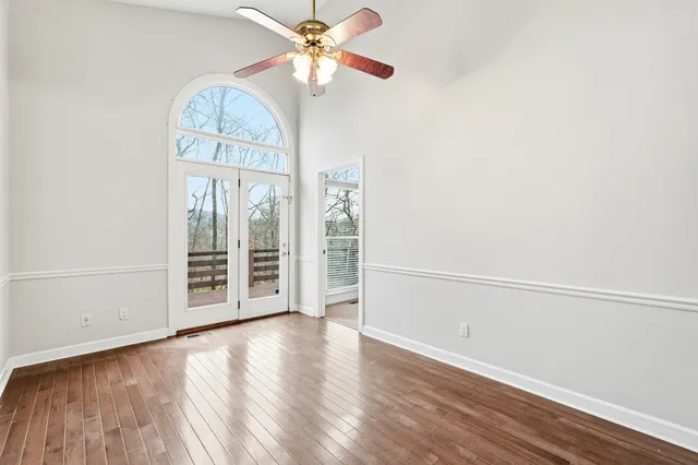 an empty room with wooden floor fan and windows