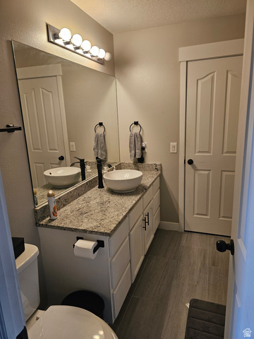 7481 Red Pine Road Eagle Mountain, UT 84005 - Photo 19 of 38 Upstairs hall bathroom with vessel sinks set into a granite-finish countertop, white cabinetry with matte black hardware, a large vanity mirror, and wood-look flooring