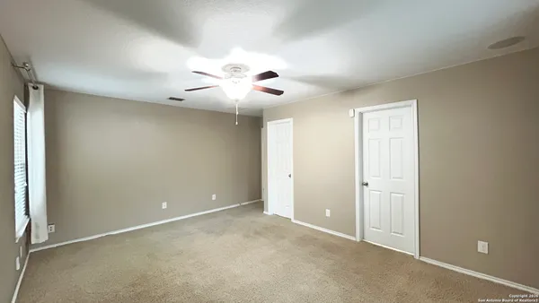an empty room with chandelier fan and windows