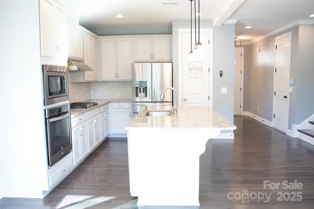 a large white kitchen with stainless steel appliances kitchen island granite countertop a refrigerator a sink a stove and white cabinets with wooden floor