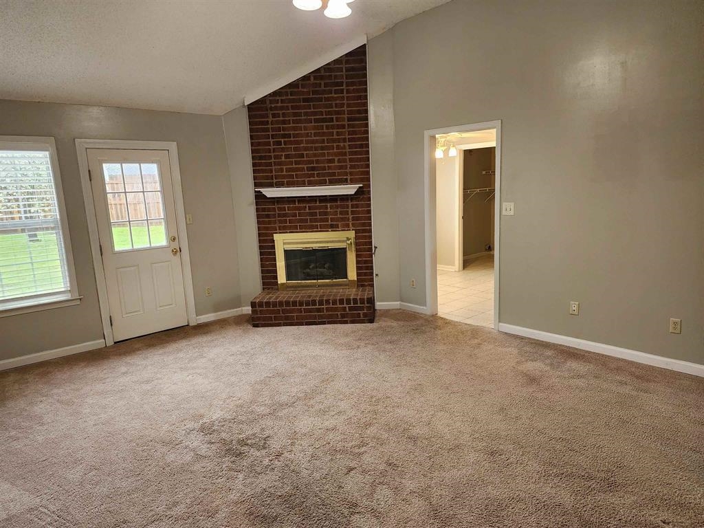 255 Windy Ridge Cove Collierville, TN 38017 - Photo 2 of 21 Unfurnished living room featuring a brick fireplace, vaulted ceiling, and light carpet