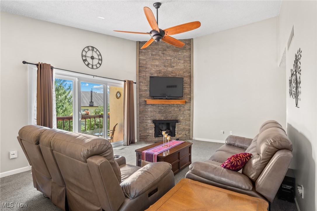 889 Hampton Ridge Drive Akron, OH 44313 - Photo 14 of 38 Living room featuring a textured ceiling, ceiling fan, a stone fireplace, and carpet floors