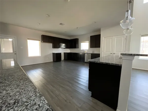 a living room with stainless steel appliances kitchen island granite countertop a stove a refrigerator a sink a microwave with wooden floors and cabinets