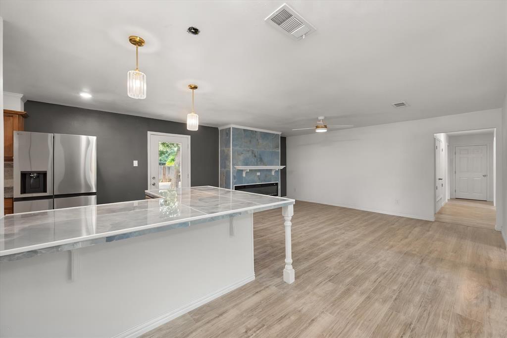 3400 Emhouse Road Corsicana, TX 75110 - Photo 17 of 34 Open-concept space featuring wood-finish flooring, a white kitchen island with a stone-finish countertop, stainless steel refrigerator, and a fireplace with a stone-finish surround