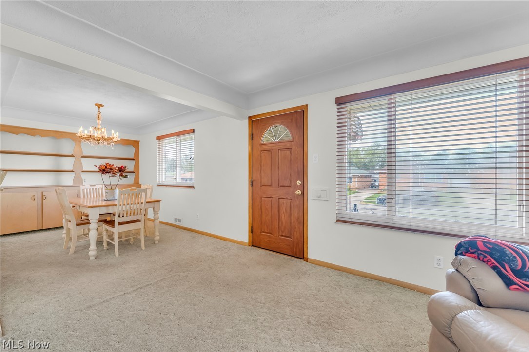 3023 Norris Avenue Cleveland, OH 44134 - Photo 3 of 41 Carpeted living area featuring a prominent wood entry door with an arched glass insert, alongside a dining space with an ornate chandelier and built-in shelving