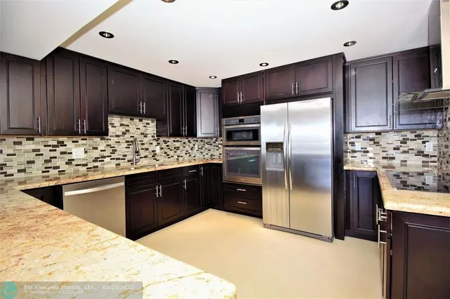 a kitchen with stainless steel appliances kitchen island granite countertop a sink refrigerator and cabinets