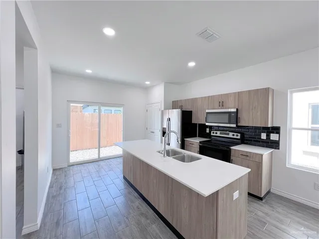 a kitchen with stainless steel appliances a sink a stove a refrigerator with wooden floor and cabinets