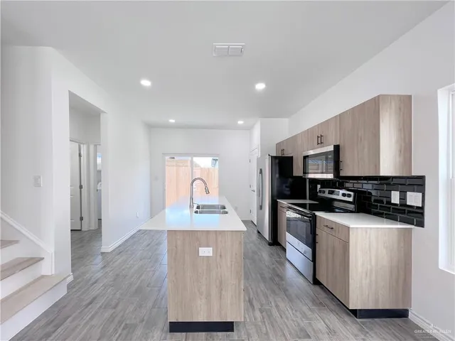 a kitchen with stainless steel appliances a stove top oven a refrigerator a sink and dishwasher with wooden floor