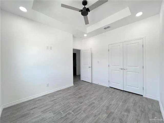 an empty room with wooden floor ceiling fan and windows