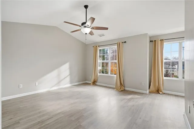 an empty room with wooden floor fan and windows