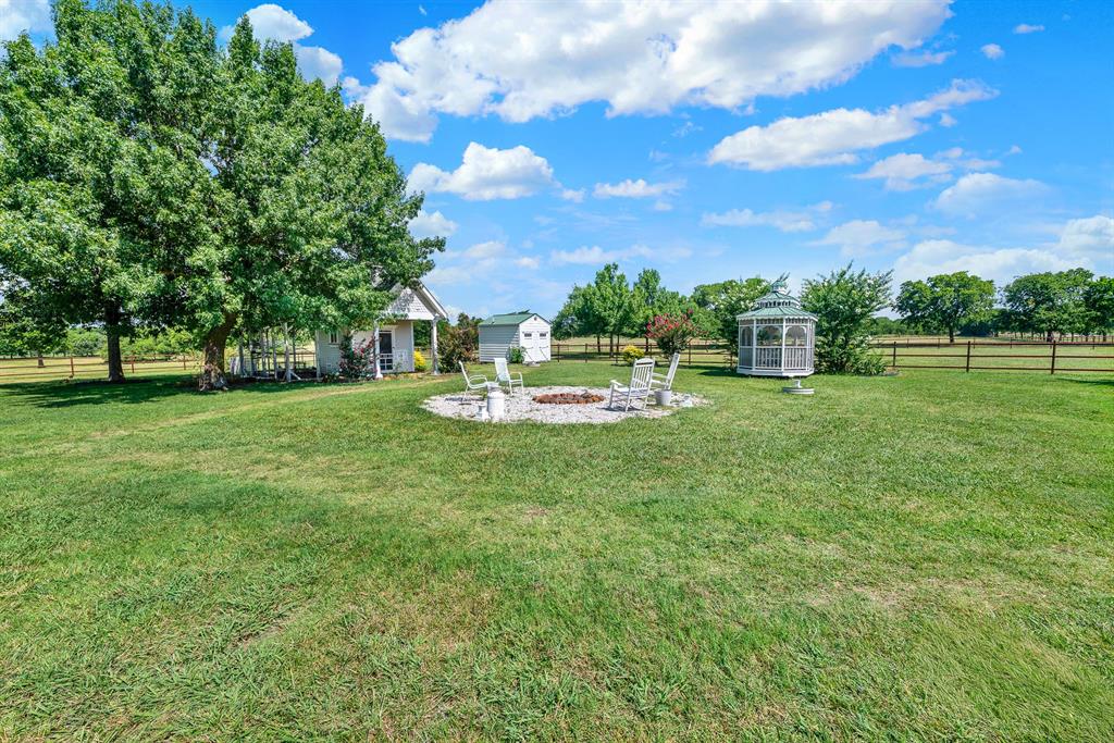 1425 Lone Star Road Celina, TX 75009 - Photo 35 of 40 The beautifully maintained grounds offer inviting spaces to relax and gather, centered around a welcoming fire pit surrounded by open lawn and peaceful country views. A charming gazebo provides the perfect spot for morning coffee or evening conversations, while the historic pump house adds character and serves as a reminder of the property's heritage. A convenient storage shed offers additional space for equipment and tools, completing this thoughtfully designed outdoor setting that blends function with timeless country charm.