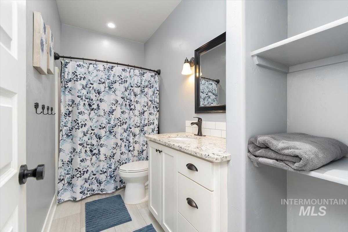 15015 Leon Lane Caldwell, ID 83607 - Photo 19 of 44 Bathroom featuring a white vanity with a granite-style countertop, subway tile backsplash, and dark bronze fixtures