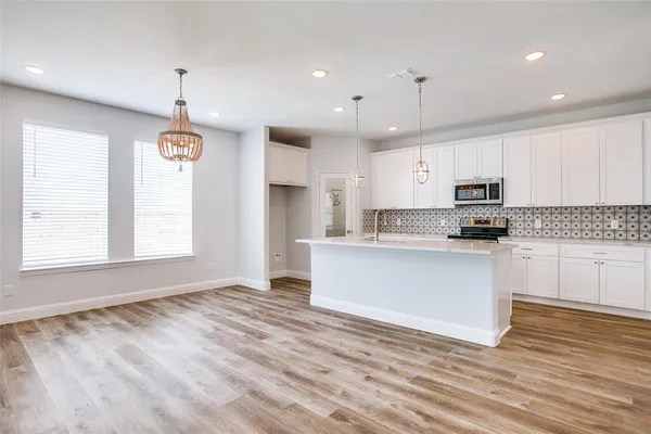 a kitchen with granite countertop a stove a sink and white cabinets with wooden floor