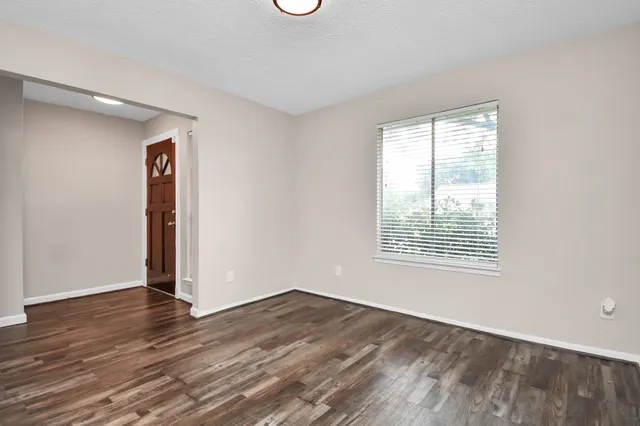 a view of an empty room with wooden floor and a window