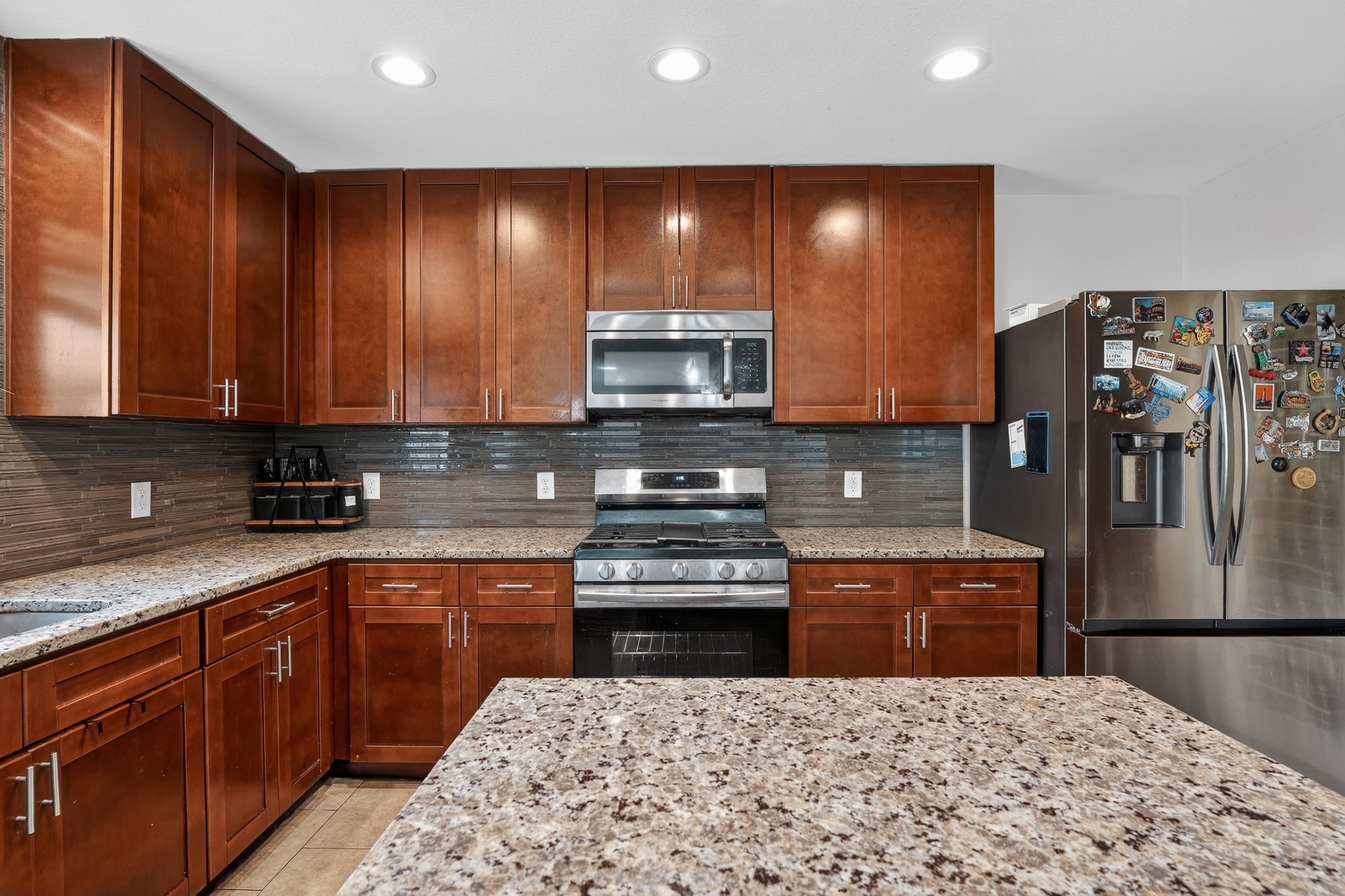 816 Rusk Road Round Rock, TX 78665 - Photo 16 of 29 Kitchen featuring wood cabinetry, light-toned speckled countertops, a mosaic tile backsplash, and stainless steel appliances including a range, microwave, and refrigerator