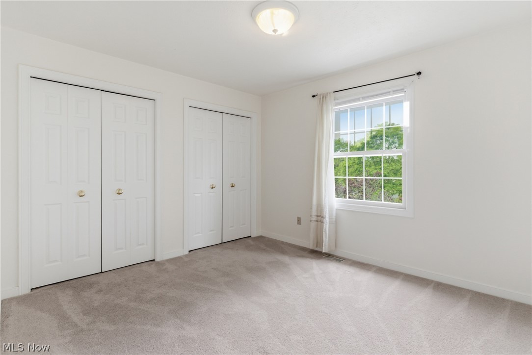 11678 Dunham Road Northfield, OH 44067 - Photo 26 of 38 Carpeted room featuring two bifold door closets, a window with white trim, and a flush mount ceiling light fixture