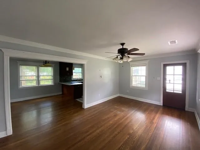 an empty room with wooden floor chandelier fan and windows