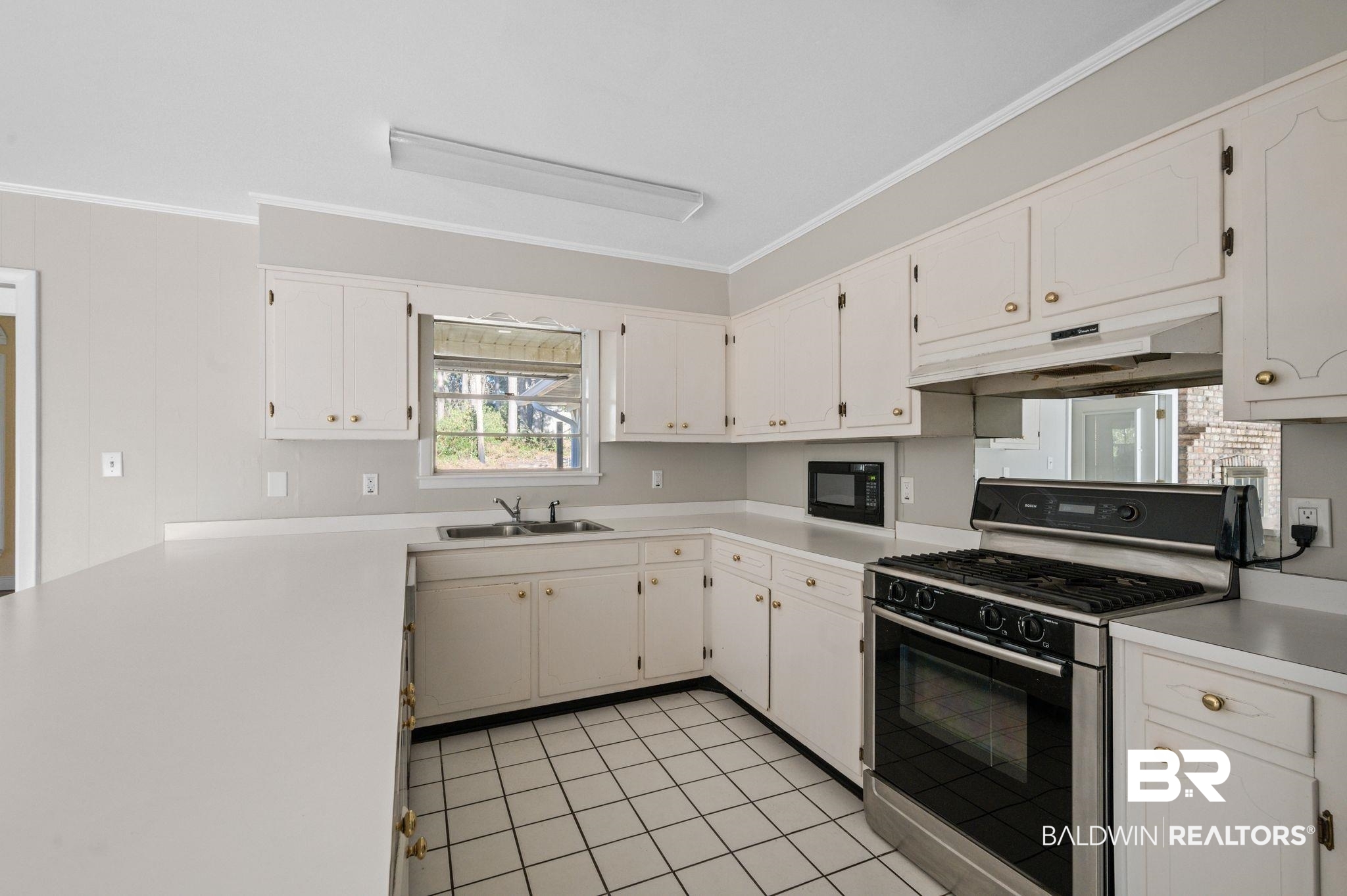 909 Caroline Avenue Daphne, AL 36526 - Photo 24 of 46 Kitchen featuring gas stove, black microwave, sink, light tile patterned floors, and white cabinets