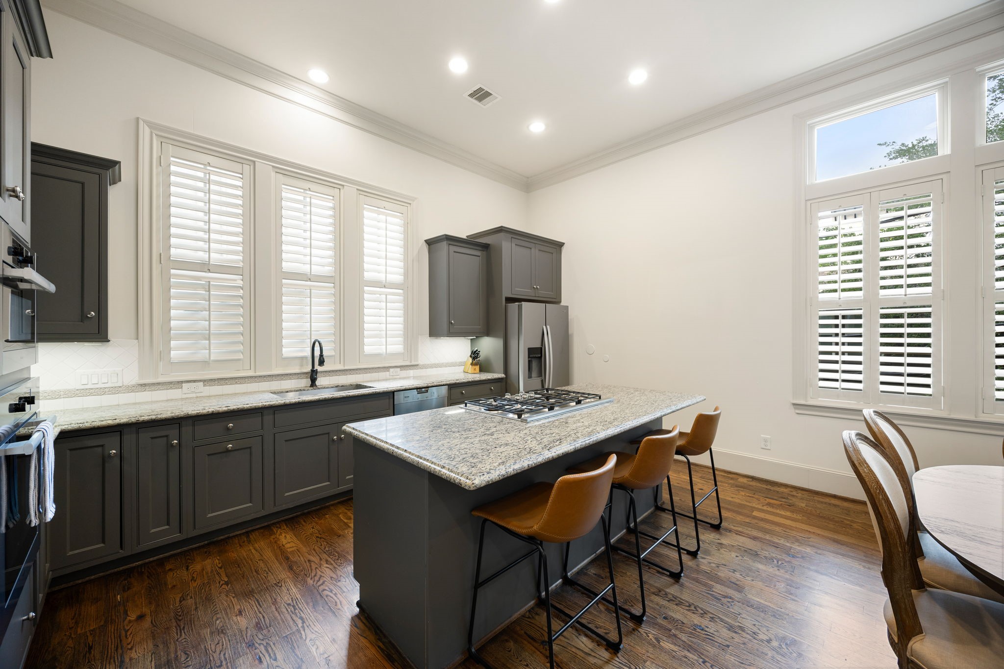 310 West Bell Street Houston, TX 77019 - Photo 22 of 44 This kitchen features elegant custom painted cabinetry, a spacious island with a built-in cooktop, and modern stainless steel appliances. Bright and airy, it has large windows with shutters and warm hardwood floors, creating a welcoming atmosphere.