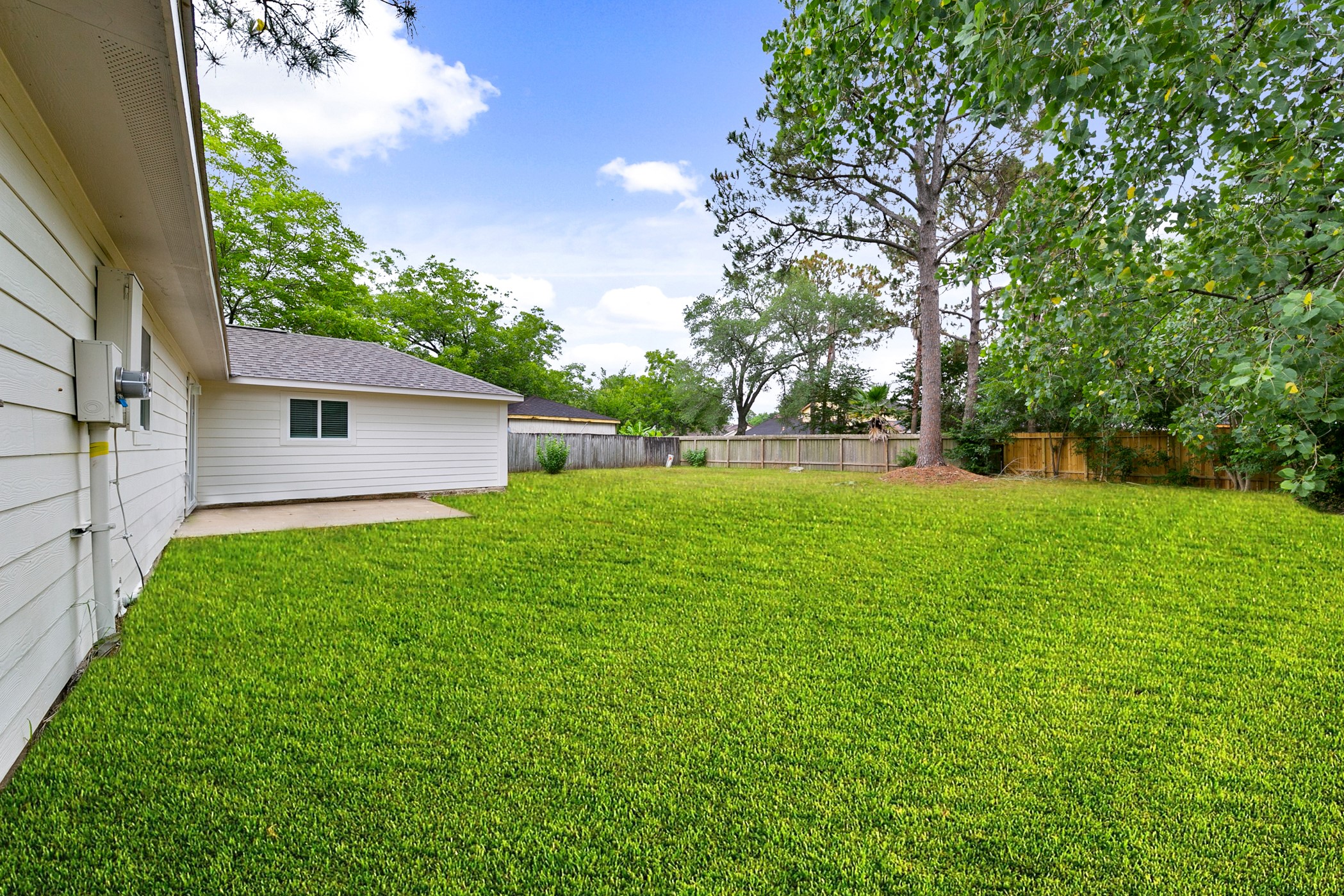 6811 McCullum Road Houston, TX 77489 - Photo 20 of 22 Spacious backyard with lush green lawn, mature trees, and a wooden fence for privacy. The side of a house with light-colored siding is visible, offering a serene outdoor space.
