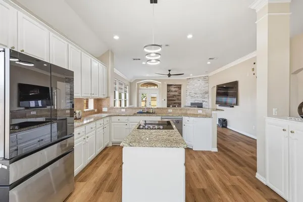 a large kitchen with stainless steel appliances granite countertop a stove top oven a sink dishwasher and white cabinets with wooden floor