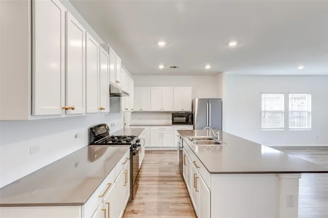 a kitchen with a sink a stove a refrigerator and white cabinets with wooden floor