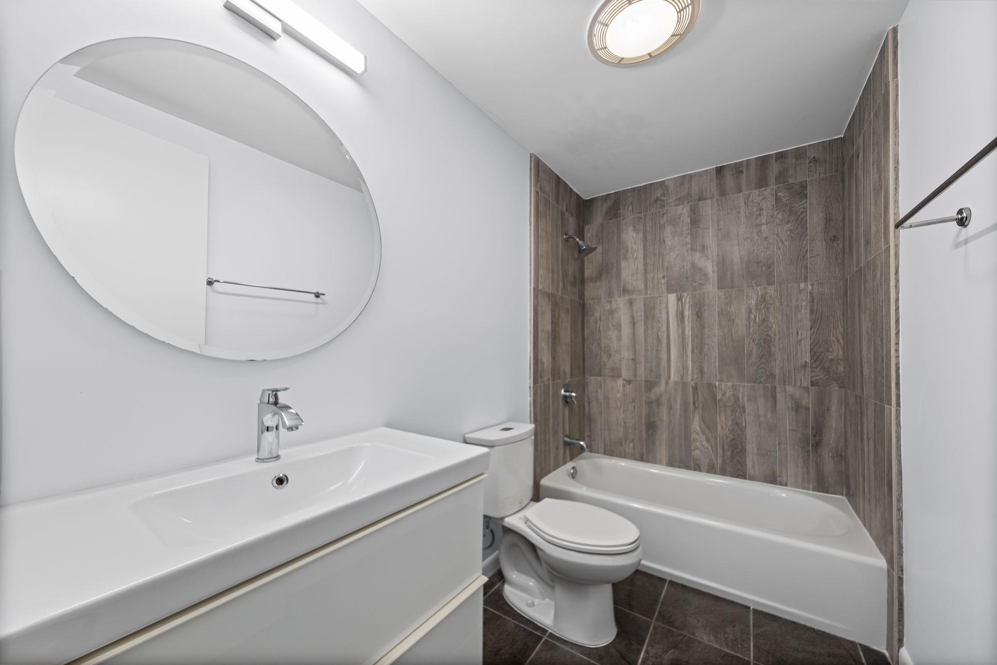 448 Tennessee Street Memphis, TN 38103 - Photo 13 of 39 Contemporary bathroom featuring a white vanity with integrated sink, a large oval mirror, and a tub-shower combination with wood-look tile surround