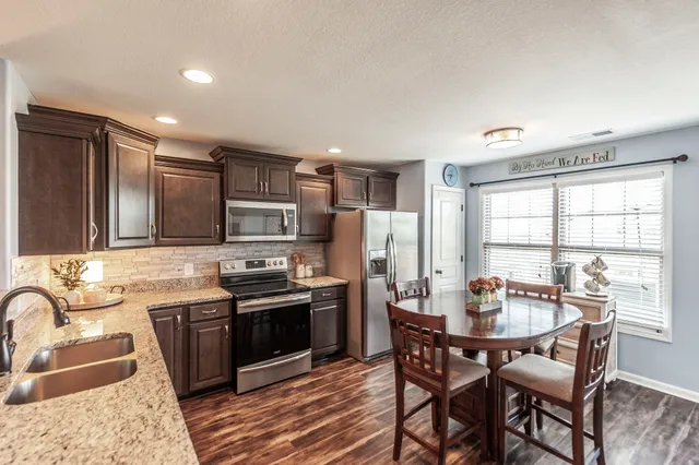 a kitchen with stainless steel appliances granite countertop a stove top oven a sink dishwasher a dining table and chairs with wooden floor