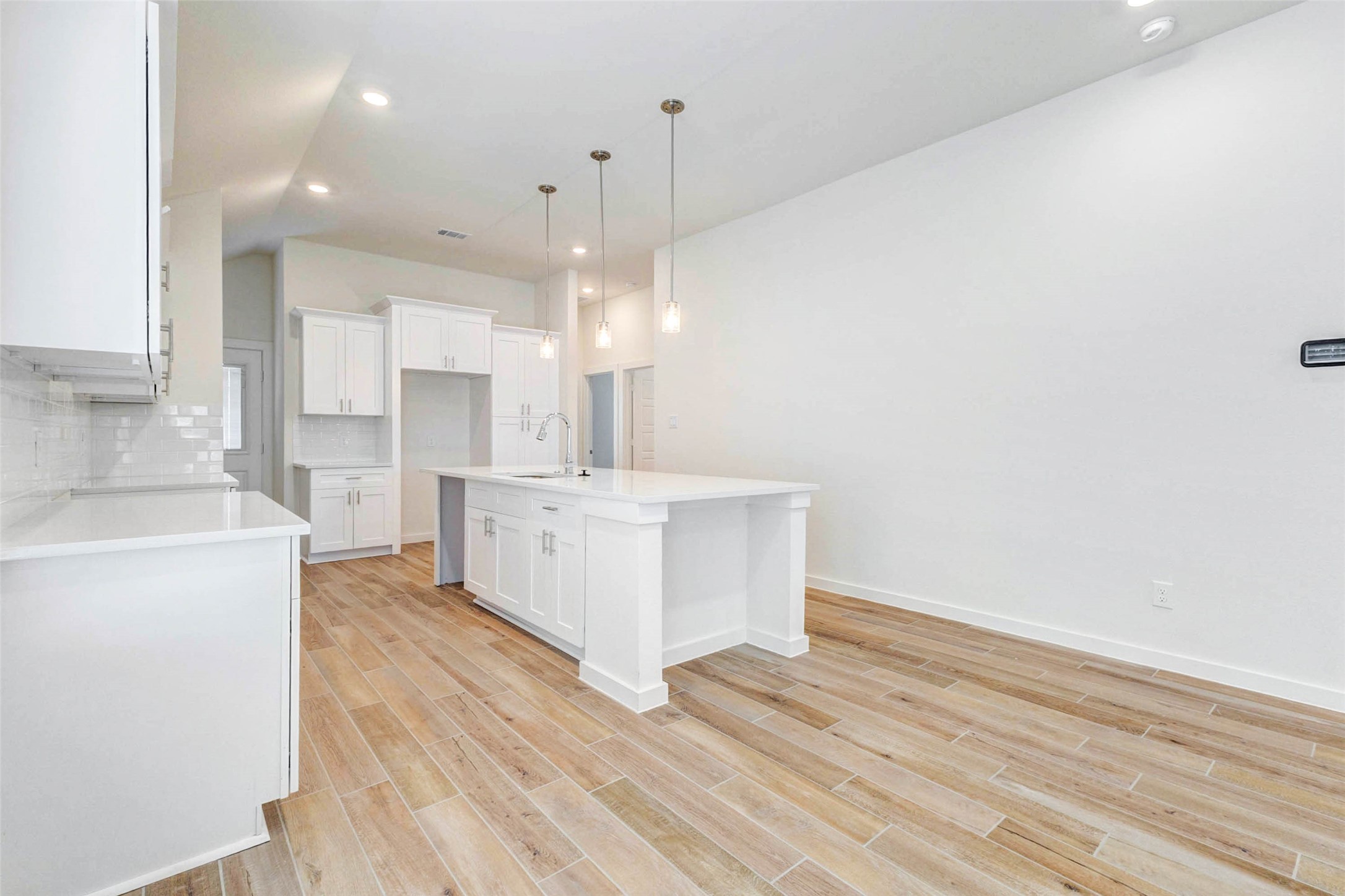6463 Escondido Drive Rosharon, TX 77583 - Photo 10 of 30 Open kitchen and dining area featuring wood-look tile flooring, white cabinetry, quartz countertops, pendant lighting, and a large center island. The spacious layout offers room for dining, gathering, and everyday meal prep.