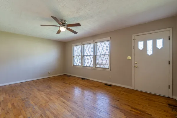 an empty room with wooden floor fan and windows