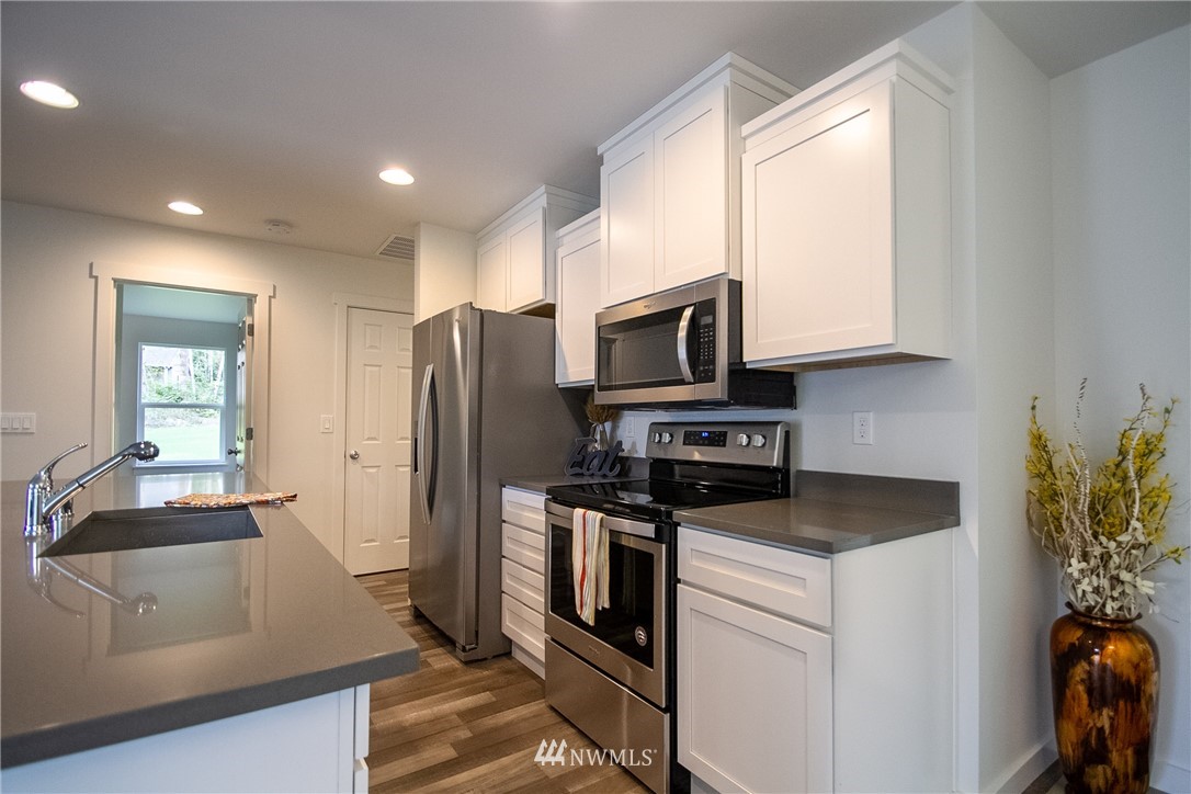 16716 Erickson Road Southwest Longbranch, WA 98351 - Photo 4 of 17 a kitchen with stainless steel appliances granite countertop a refrigerator a stove a sink and white cabinets with wooden floor