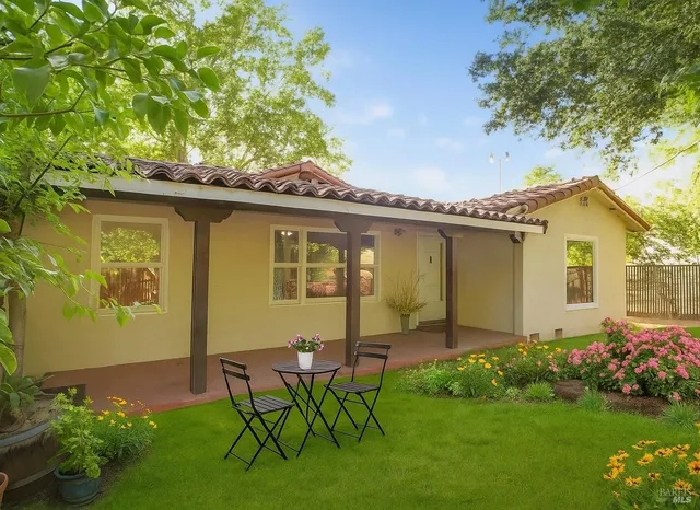 a backyard of a house with table and chairs plants and large tree