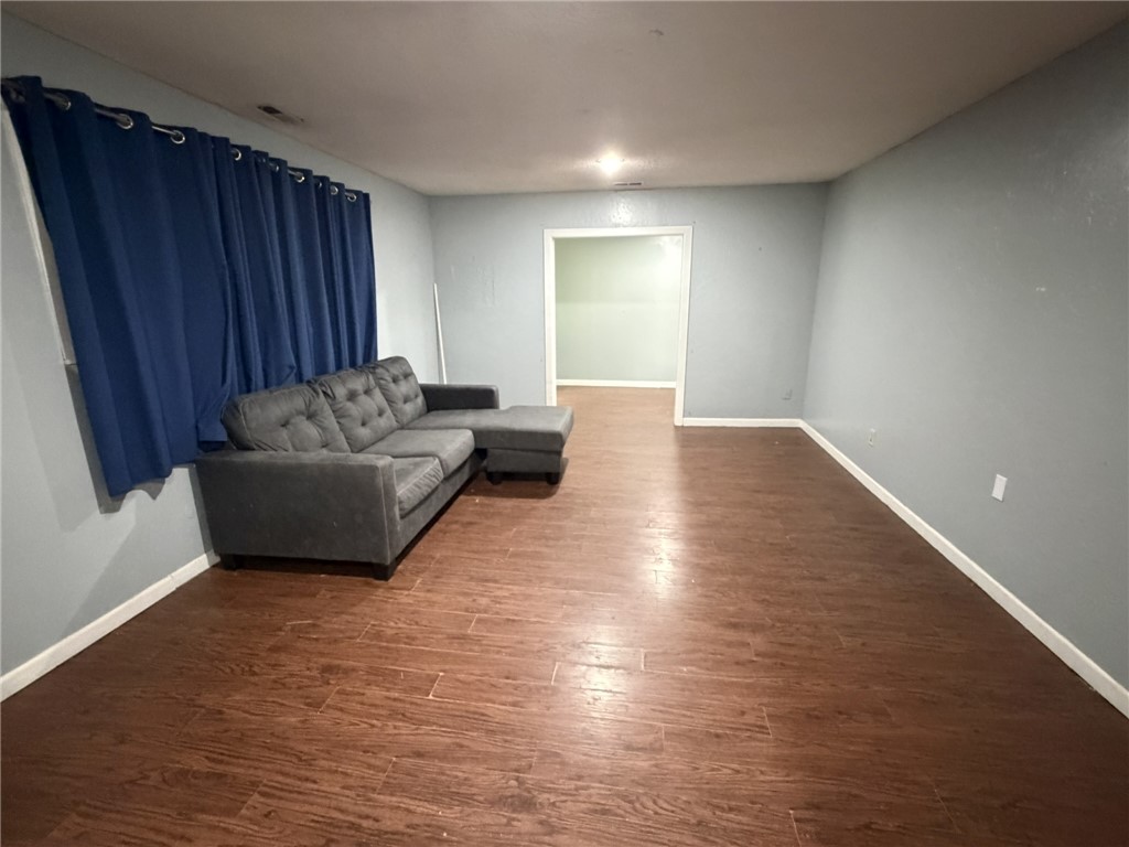 Spacious room featuring wood-finish flooring, light blue wall paint, white baseboards, and a doorway opening to an additional interior space