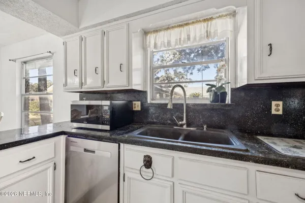 a kitchen with granite countertop a sink white cabinets and a window