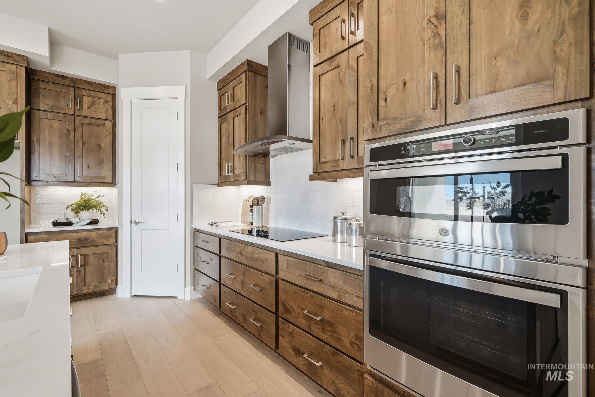 470 South Radiator Way Boise, ID 83716 - Photo 30 of 50 Modern kitchen featuring wood cabinetry, light wood-finish flooring, white countertops, built-in stainless steel double ovens, and a sleek range hood