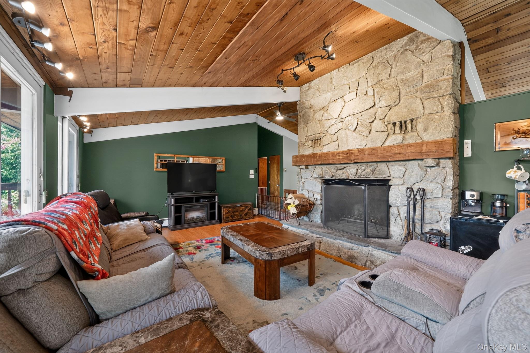 424 Laroe Road Chester, NY 10918 - Photo 37 of 43 Expansive stone fireplace with a substantial wood mantel, vaulted wood-plank ceiling, exposed white support beams, recessed lighting, and wood-finish flooring