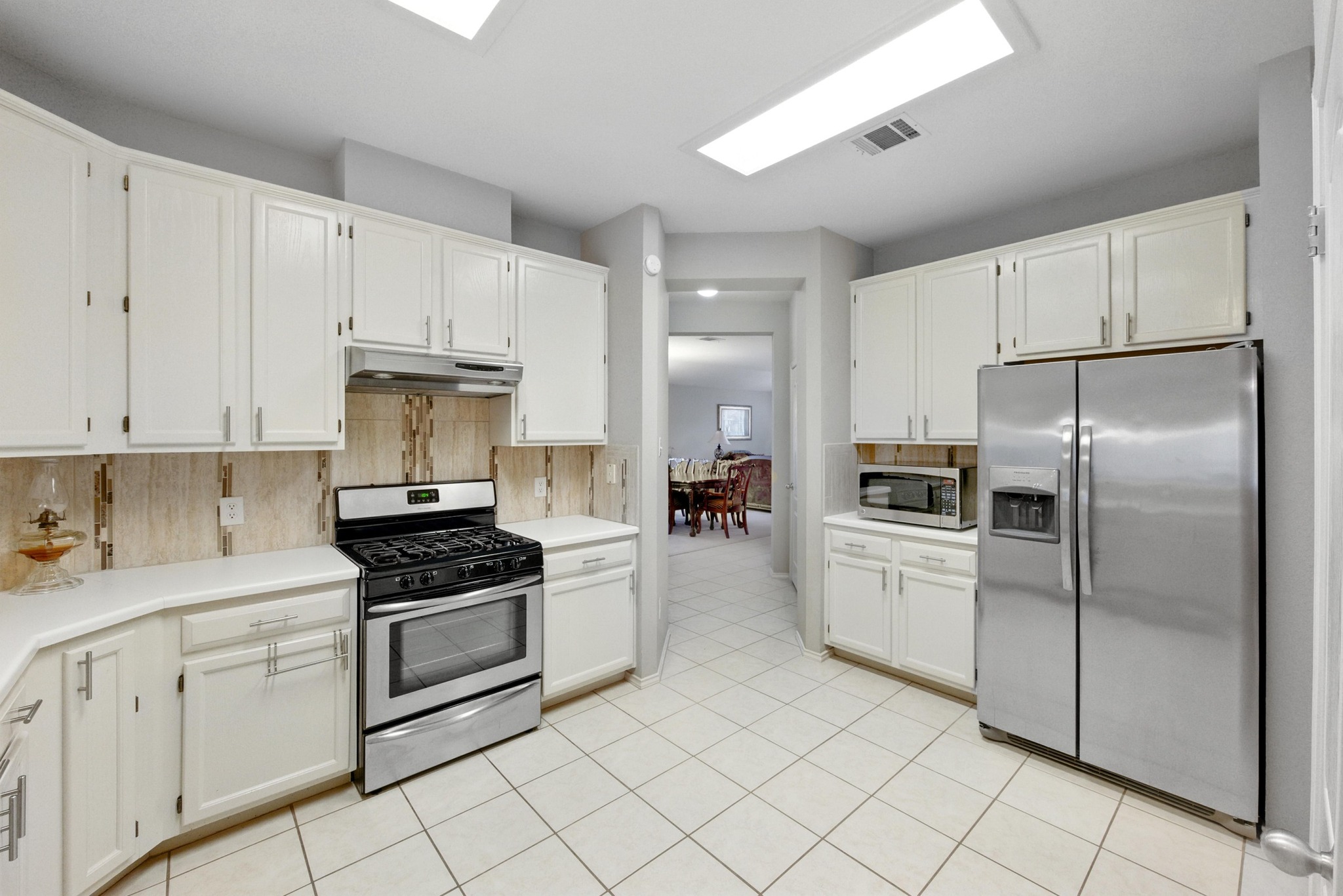 9602 Tea Rose Trail Austin, TX 78748 - Photo 11 of 27 Kitchen featuring stainless steel appliances, light countertops, white cabinetry, backsplash, and light tile patterned floors