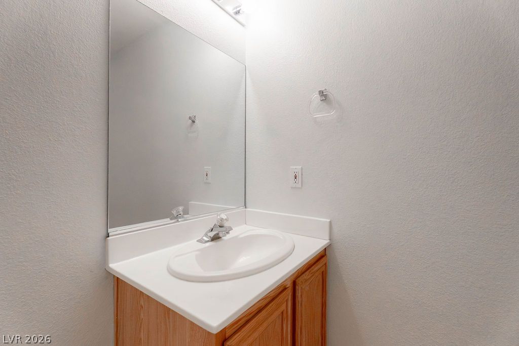 8379 Rockefeller Street Las Vegas, NV 89123 - Photo 18 of 36 A classic wood vanity with a white integrated sink basin rests against neutral textured walls.