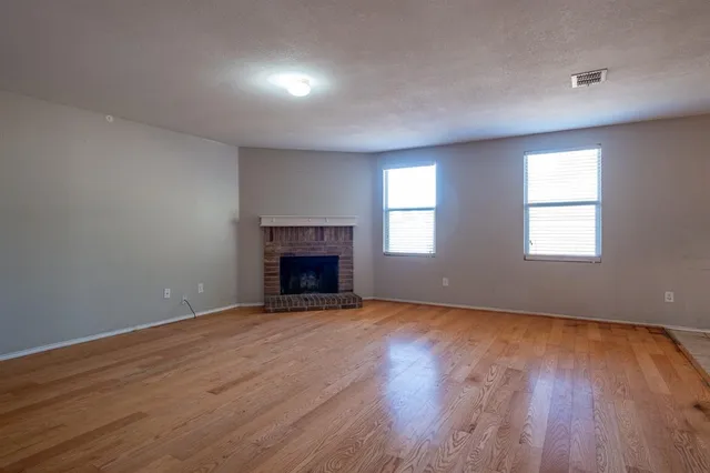 an empty room with wooden floor fireplace and windows