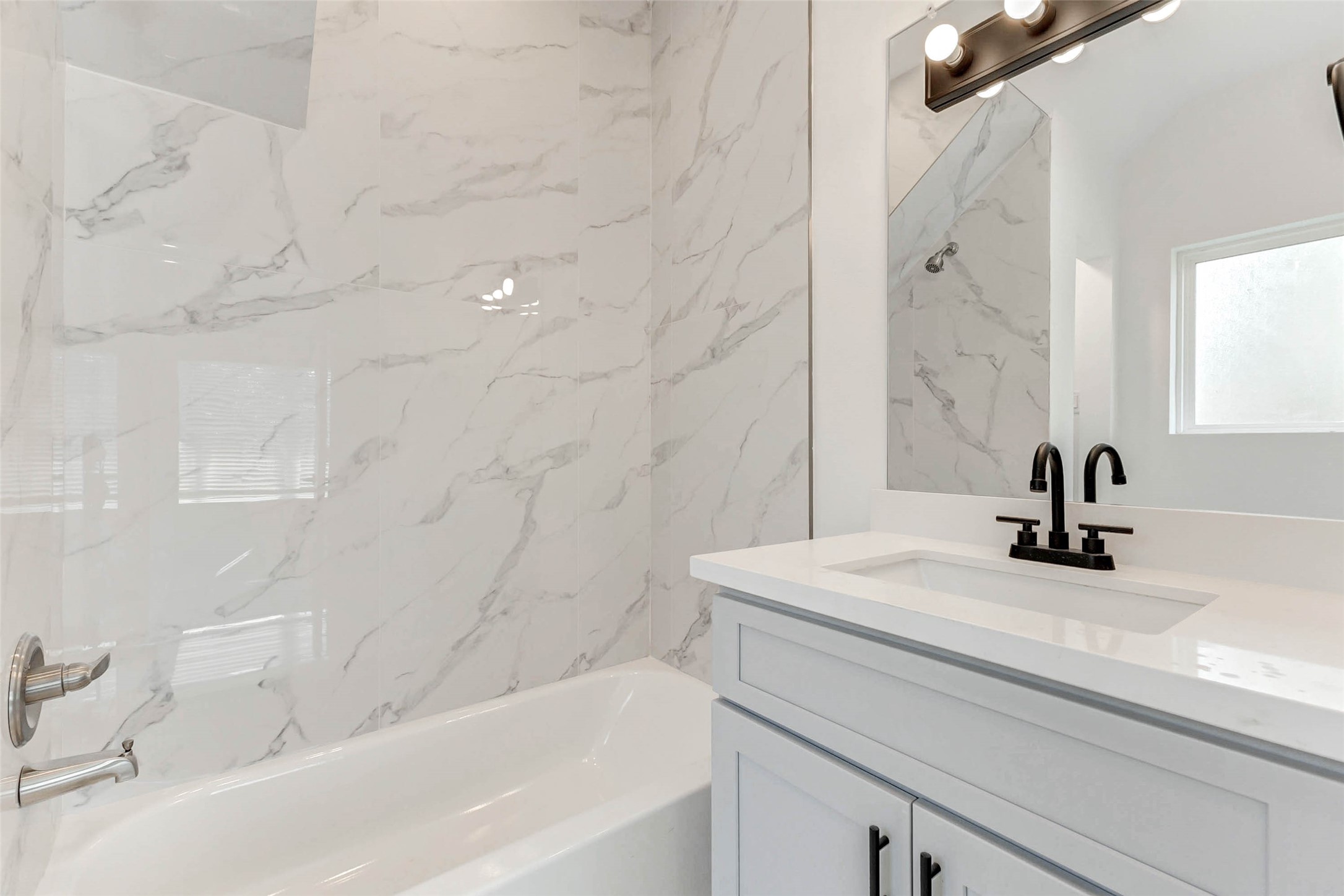 6017 Beall Street Houston, TX 77091 - Photo 22 of 33 Contemporary elegance shines in this full bath, complete with a quartz-topped vanity, bold matte black fixtures, and full-height marble-style tile that elevates everyday routines.