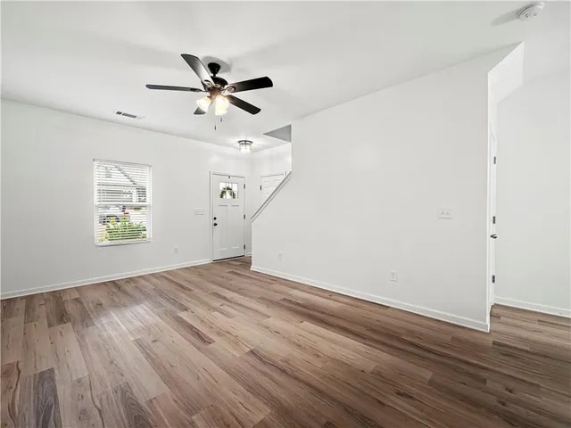 an empty room with wooden floor ceiling fan and windows