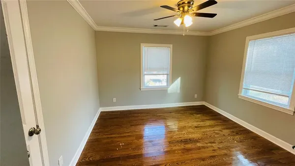 an empty room with wooden floor fan and windows