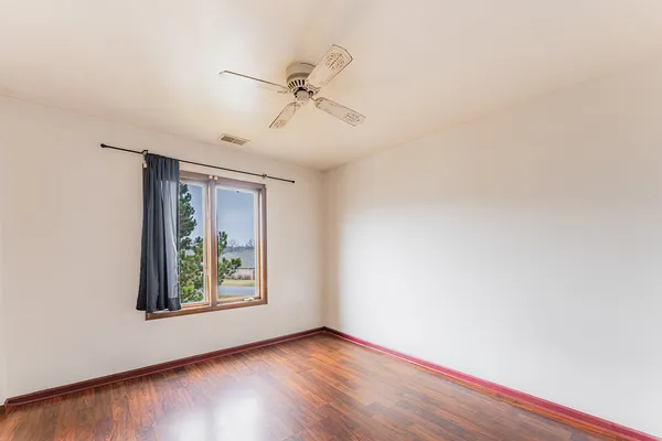 an empty room with wooden floor fan and windows