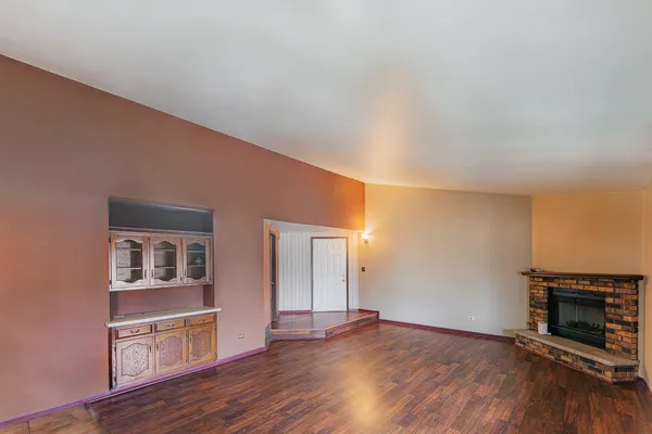 an empty room with wooden floor fireplace and cabinet