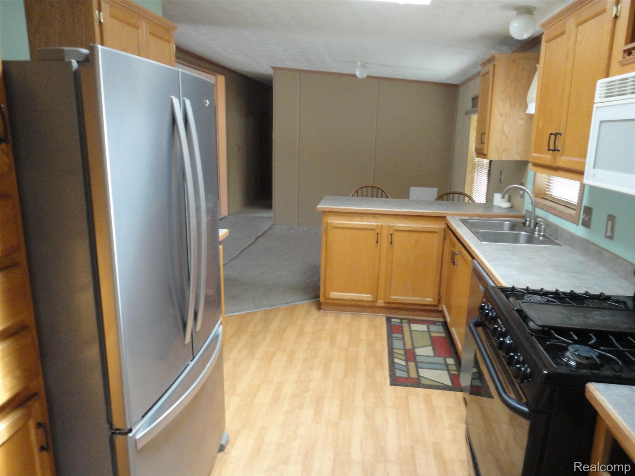 3954 Ryans Ridge Monroe, MI 48161 - Photo 11 of 28 Kitchen featuring wood-finish flooring, light wood cabinetry, stainless steel refrigerator, black gas range, and a breakfast bar