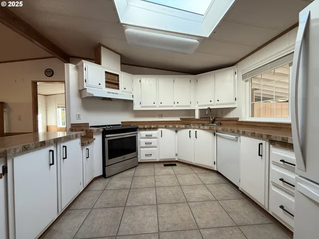 a large kitchen with stainless steel appliances granite countertop a stove top oven a sink dishwasher and white cabinets